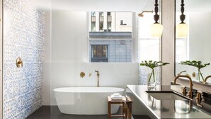 Une salle de bain moderne avec une baignoire sur pieds, un meuble-lavabo avec un miroir et une fenêtre offrant une vue sur le bâtiment extérieur.