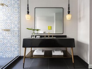 Un baño moderno con tocador negro, un espejo grande, dos luces empotradas en la pared y un estante con toallas dobladas.