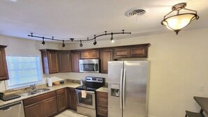 A modern kitchen with wooden cabinets, stainless steel appliances, a microwave, a refrigerator, and a dining area with a table and chairs. - Perfect extended stay! (Biloxi)