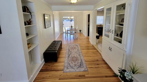 A hallway with wooden flooring, a patterned rug, a bench, and white shelving units with decorative items. - Perfect extended stay! (Biloxi)