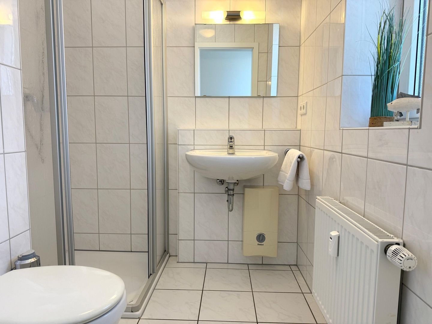 Ein Badezimmer mit Toilette, Waschbecken, Dusche und Handtuchwärmer.