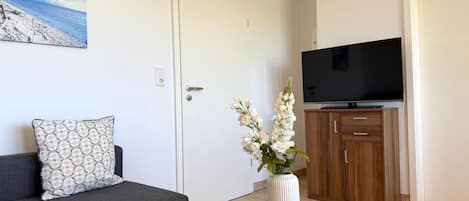 A living room with a sofa, a glass coffee table, a vase with flowers, a television, and a wooden cabinet.