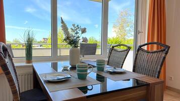 A dining area with a glass table, wicker chairs, and a view of greenery outside.