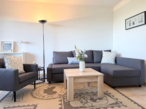 Ein modernes Wohnzimmer mit einem grauen Sofa, einem passenden Sessel, einem Holztisch und einer Stehlampe.
