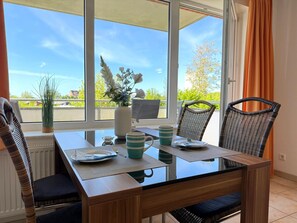 Un coin repas avec une table en verre, des chaises en osier et une vue sur la verdure environnante.