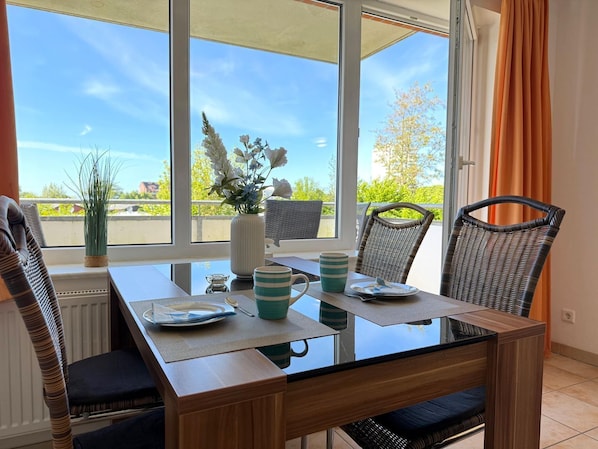 A dining area with a glass table, wicker chairs, and a view of greenery outside.