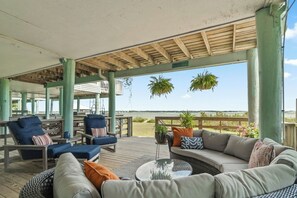 A covered outdoor seating area with a view of the water, featuring a sofa, chairs, and hanging planters. - Sandcastle Shores - Navarre Beach Waterfront (Navarre)