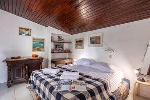 Een slaapkamer met een houten plafond, een bed met een geruit plaid, een bureau met een kom en diverse ingelijste foto's aan de muren.