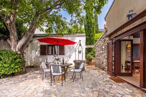 Un patio de piedra con una mesa, sillas, un paraguas rojo y un muro de piedra.