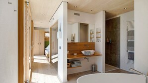 Une salle de bain moderne avec une baignoire sur pieds, des étagères en bois, un grand miroir et un mur en pierre.