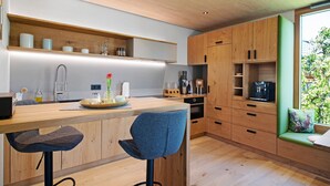 Une cuisine moderne avec des meubles en bois, un coin bar et un petit espace détente près d’une fenêtre.