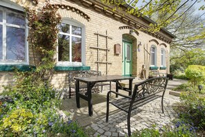 Un bâtiment en briques avec une porte verte, une fenêtre et une table avec des bancs à l’extérieur.