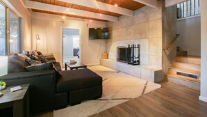 Een moderne woonkamer met een open haard, houten balken in het plafond en een trap.