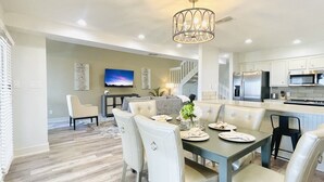 A modern kitchen with stainless steel appliances, a dining area with a table set for four, and a living room with a sofa and a TV.