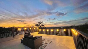 A rooftop terrace with a curved wooden railing, a seating area with cushions, and string lights.