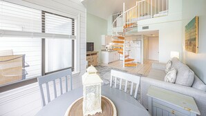 Un amplio espacio habitable con una mesa de comedor, un sofá, una escalera y una cocina al fondo.
