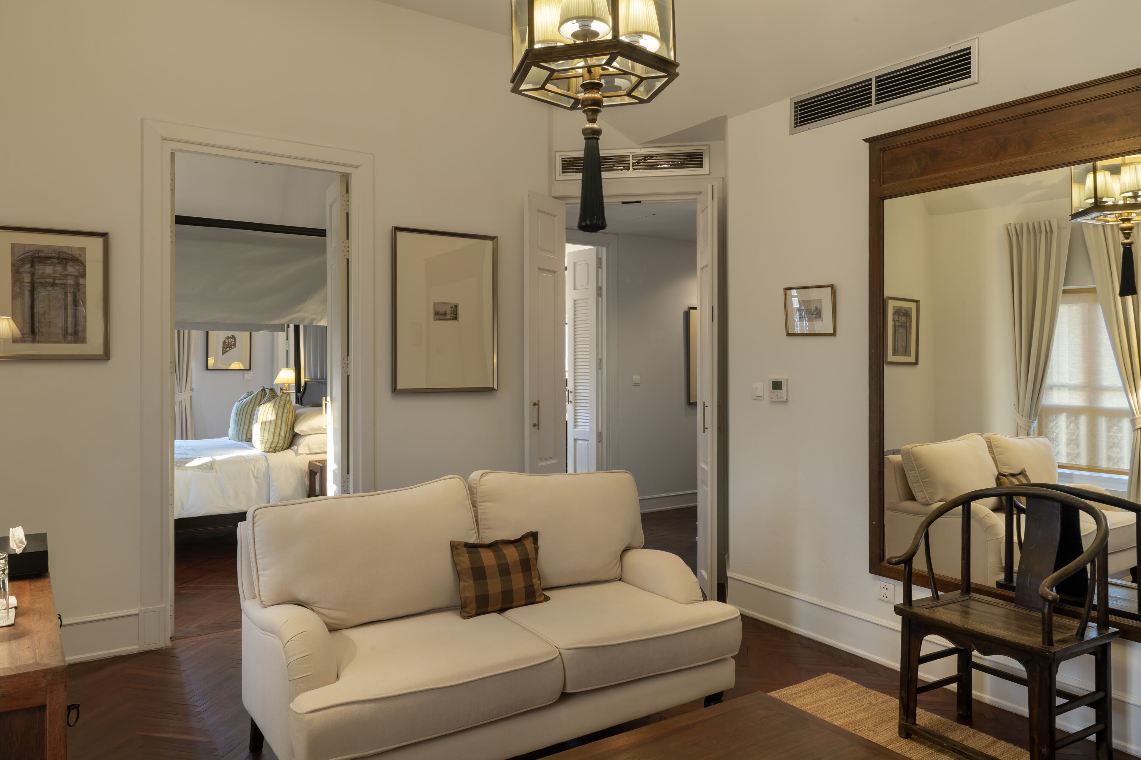 A living room with a sofa, a wooden chair, a large mirror, and a ceiling light fixture.