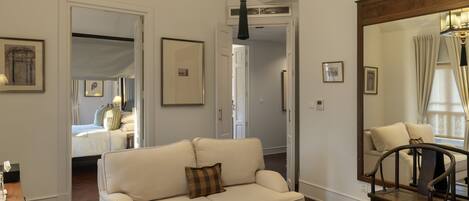 A living room with a sofa, a wooden chair, a large mirror, and a ceiling light fixture.