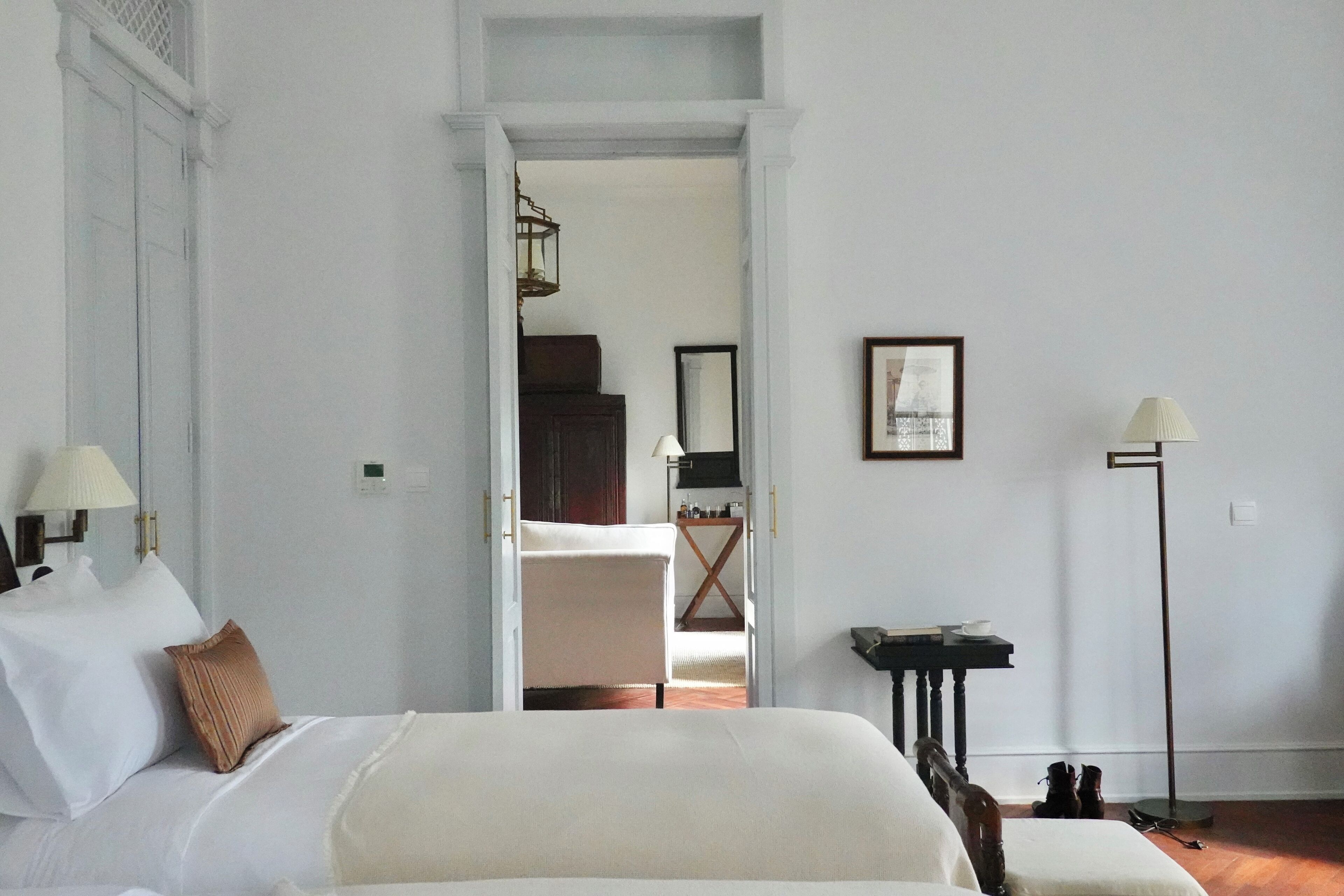 A hotel room with a large bed, a desk, a chair, a floor lamp, and a mirror on the wall.