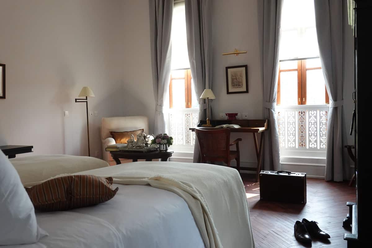 Una habitación de hotel con dos camas, un escritorio, una silla, una lámpara y una ventana con cortinas.