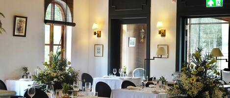 A dining area with tables set for a meal, framed pictures on the walls, and a large window with natural light.