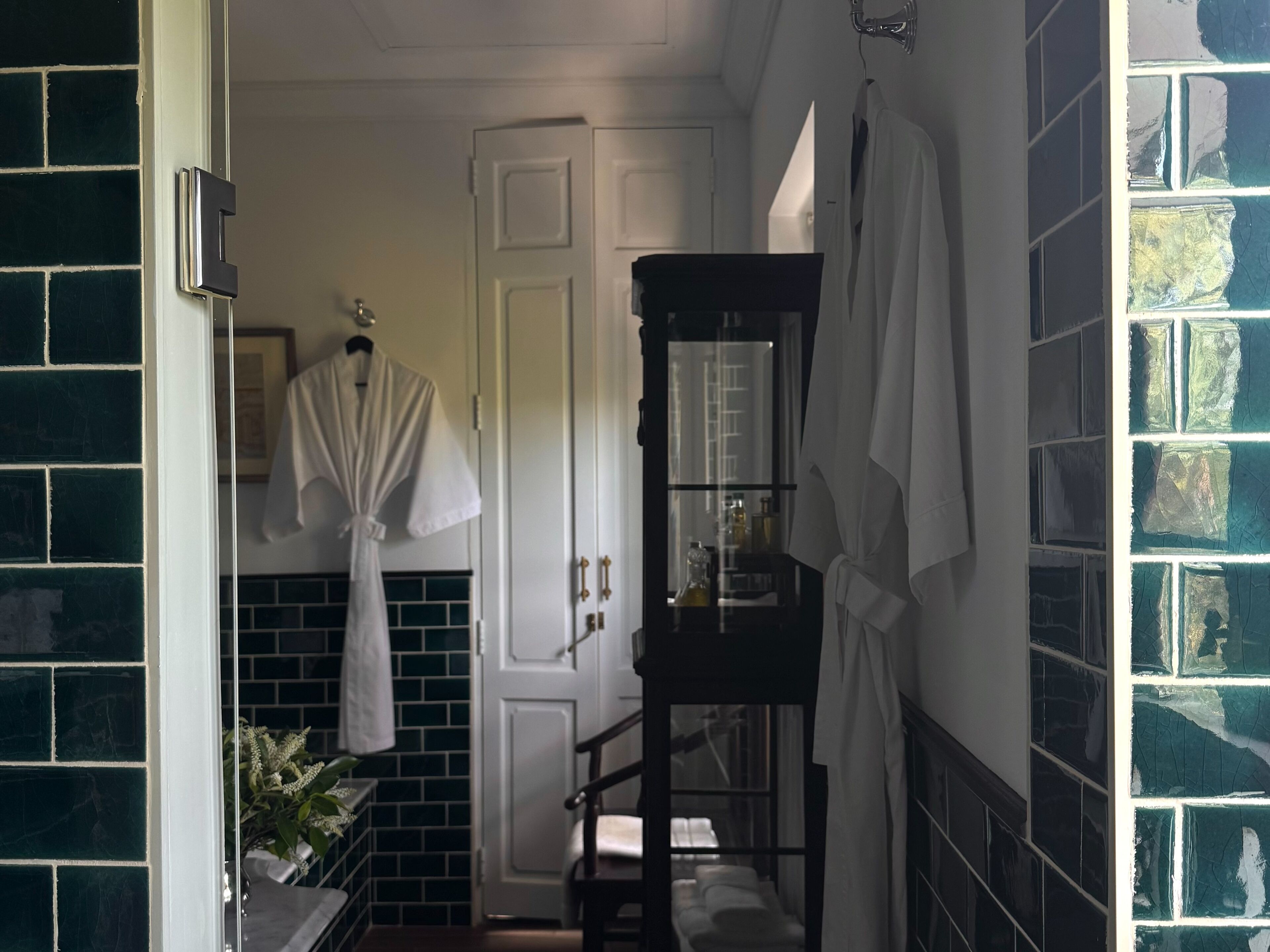A bathroom with a tiled floor, a white door, a mirror, and a shelf with toiletries.