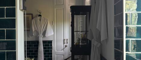 A bathroom with a tiled floor, a white door, a mirror, and a shelf with toiletries.