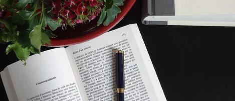 Un libro abierto con un bolígrafo encima, junto a un cuenco rojo con flores.