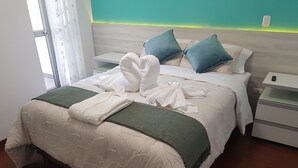 Ein ordentlich bezogenes Bett mit weißen und grünen Decken, zwei blauen Kissen und einem weißen Bademantel.