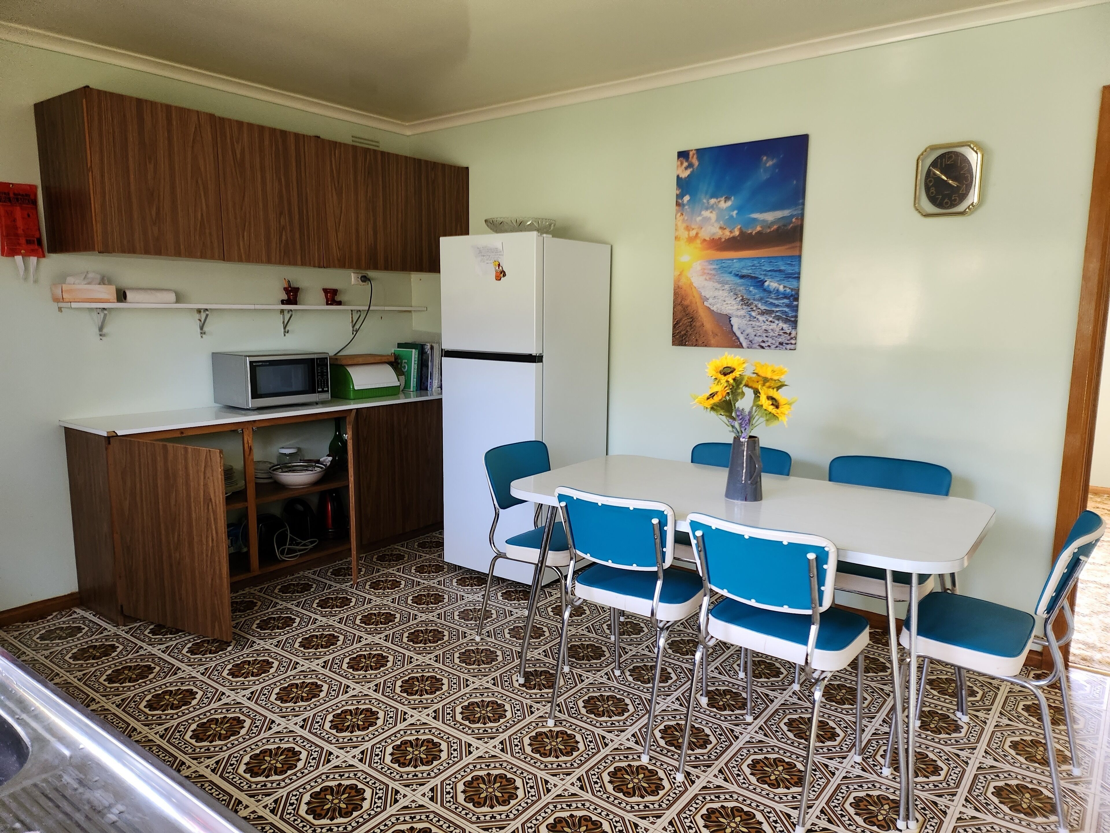 A compact kitchen with a microwave, refrigerator, and a small dining area with blue chairs and a white table.