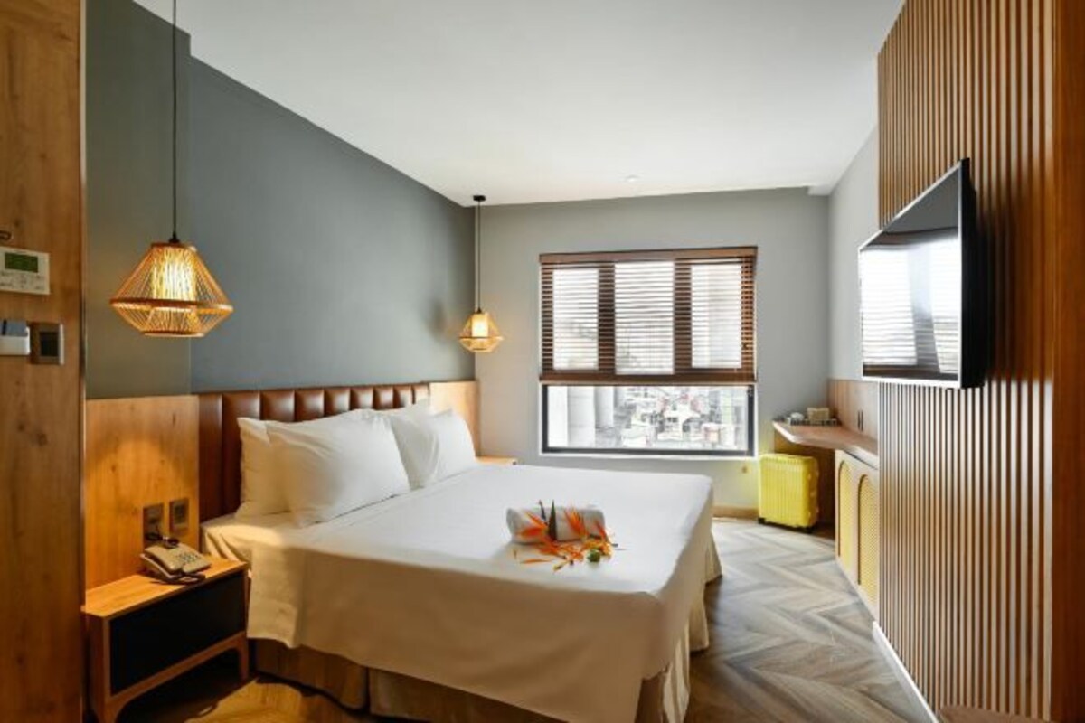 Une chambre d’hôtel avec un lit, une table de chevet, une lampe, une fenêtre et un téléviseur.