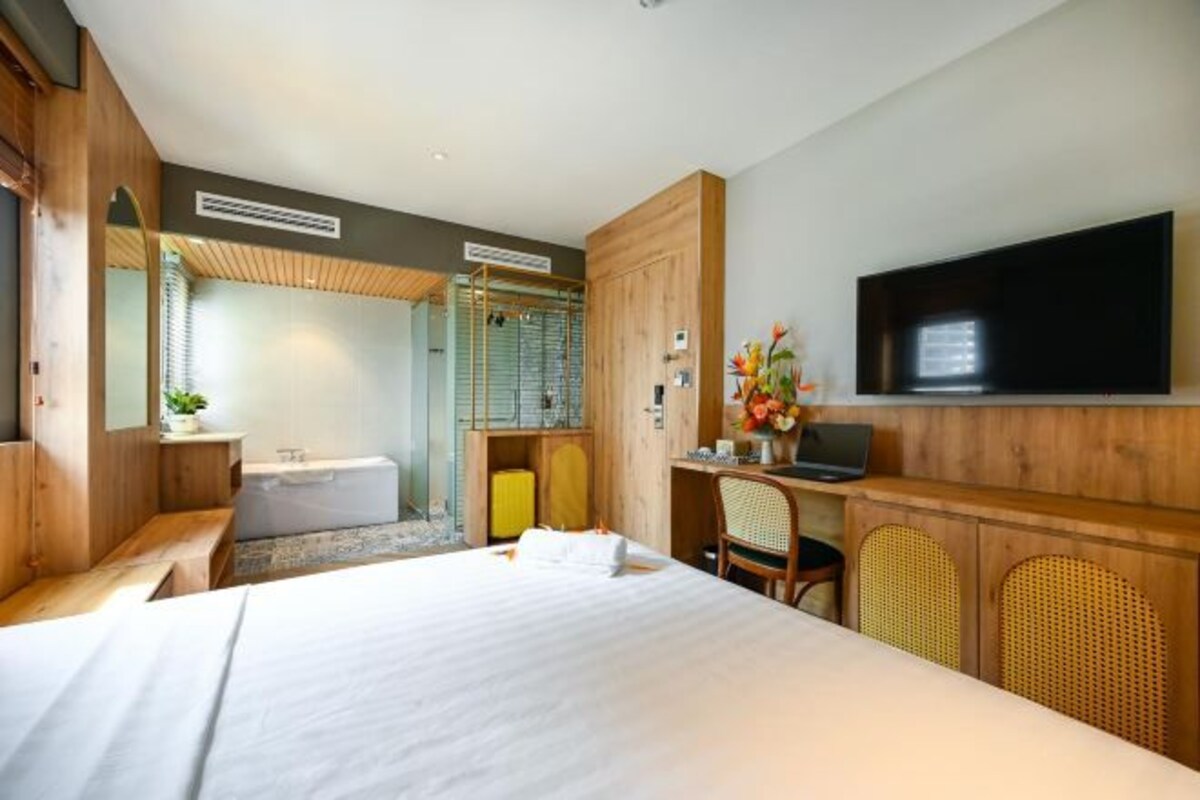 Une chambre d’hôtel moderne dotée d’un grand lit, d’un bureau avec un ordinateur, d’un téléviseur fixé au mur et d’une salle de bain visible à travers une porte ouverte.