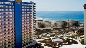 A hotel with multiple floors, a pool area, and a view of the ocean.