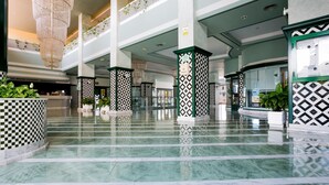 A spacious lobby with a checkered floor pattern, multiple columns with geometric designs, and hanging chandeliers.