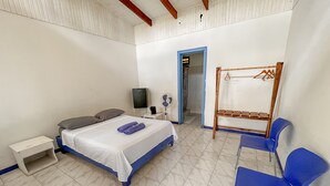 A bedroom with a bed, a bedside table, a chair, a TV, and a fan. - Hotel Exotic Lodge (Cahuita)
