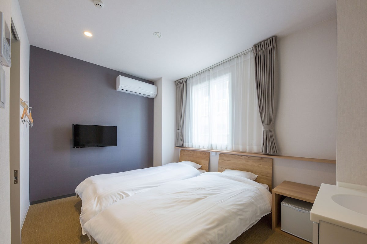 Habitación de hotel con una cama, un televisor en la pared y una ventana con cortinas.