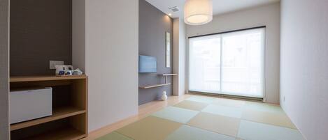 A modern, minimalist room with tatami mats, a low wooden shelf, a small white cabinet, and a large window with blinds.