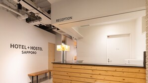 Um balcão de recepção com design em painel de madeira, um banco e uma placa indicando "RECEPTION" e "HOTEL + HOSTEL SAPPORO".
