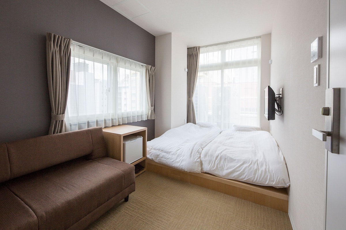 Habitación de hotel con cama, sofá, escritorio y una ventana grande con cortinas.
