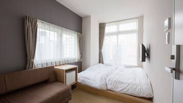 Habitación de hotel con cama, sofá, escritorio y una ventana grande con cortinas.