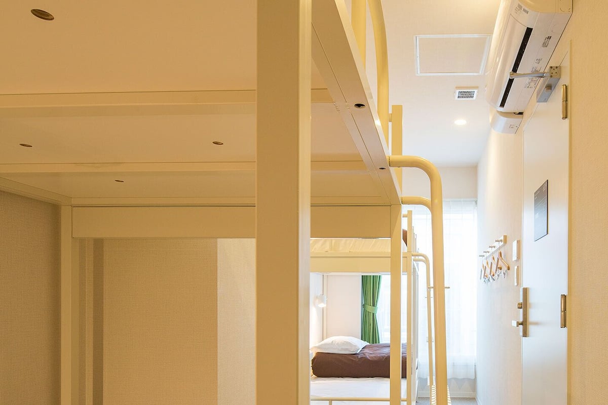Habitación con literas, una escalera, una ventana con cortinas y un aire acondicionado en la pared.