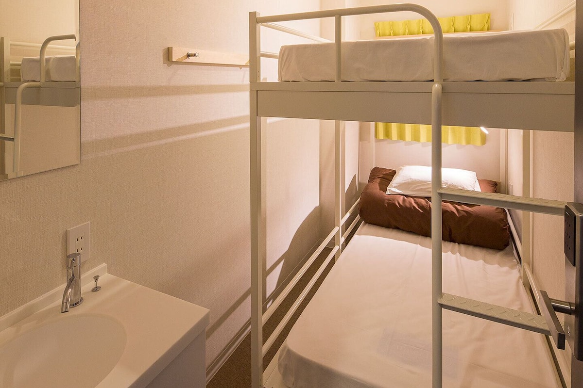 Habitación con literas, un lavabo blanco y un espejo.