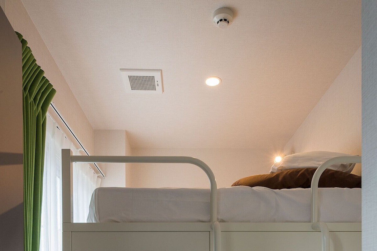 Habitación con literas, un escritorio y una silla, una ventana con cortinas e iluminación en el techo.