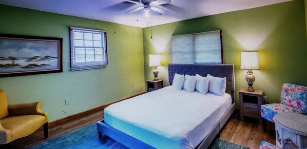A bedroom with a bed, two nightstands, a chair, a lamp, and a ceiling fan.