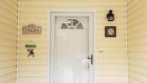 Una puerta blanca con un panel de vidrio, un buzón con el número 10604, un letrero de bienvenida adornado con flores y un cuadro con texto.