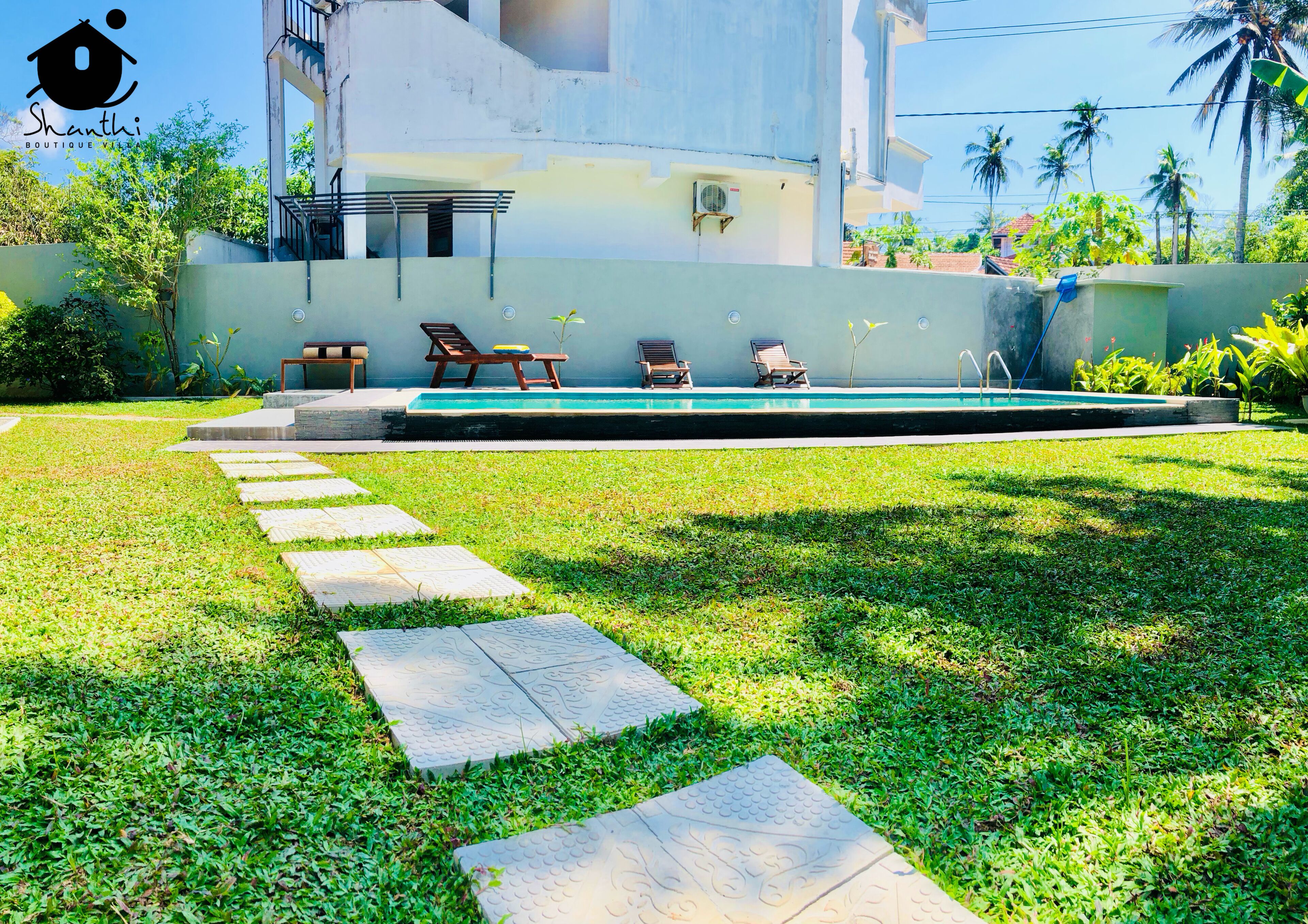 A swimming pool with lounge chairs, a stone pathway, and a building with a balcony.