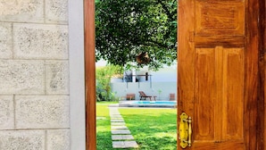 A wooden door leading to a backyard with a swimming pool, a stone pathway, and outdoor furniture. - Shanthi Boutique Villa (Hikkaduwa)