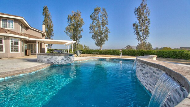 Una piscina con caída de agua, rodeada por un muro de piedra y un área de patio techada.