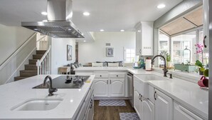 Cocina moderna con armarios blancos, una isla central, una campana extractora de acero inoxidable y una ventana con vistas al exterior.