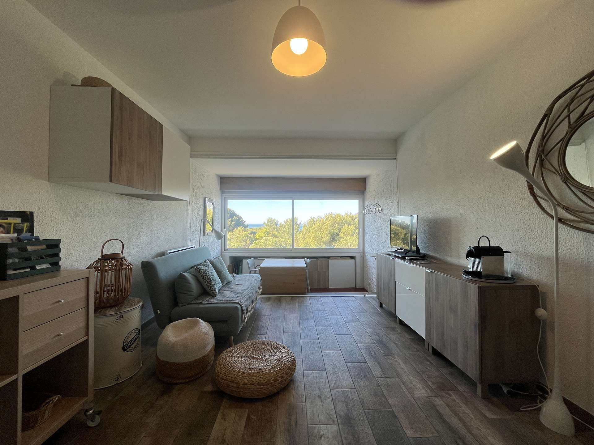 A modern kitchen and living area with a large window, wooden flooring, and a sofa.